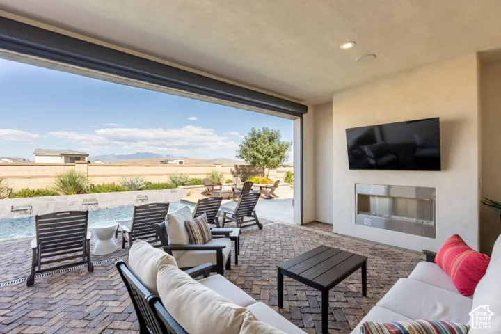 Expansive covered patio with brick paver flooring, built-in recessed fireplace, and a large roll-up door opening to the outdoors