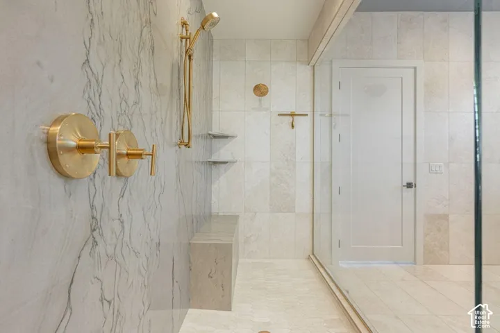 Shower with brass fixtures, a built-in bench, and tiled walls