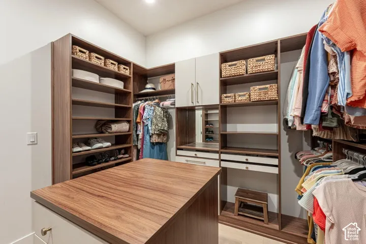 Custom built-in storage solutions with wood-finish shelving and drawers, a central island with a wood-finish countertop, recessed ceiling lighting, and a mirrored vanity area