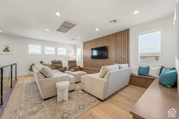 Hardwood flooring throughout, contemporary wooden slat accent wall, built-in media console, multiple windows with plantation shutters, and recessed lighting