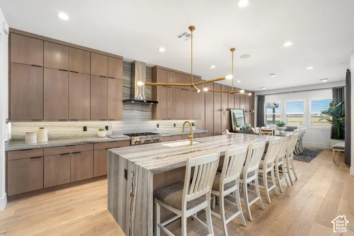Modern kitchen featuring extensive wood-finish cabinetry, a large stone-finish island with seating, integrated stainless-steel appliances, and wood-finish flooring
