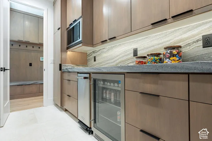 Light wood-finish cabinetry with linear hardware, under-cabinet lighting, a built-in microwave, and a beverage cooler