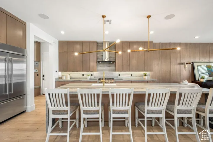 Gourmet kitchen with stainless steel refrigerator, integrated range hood, light wood-finish cabinetry, and a large central island