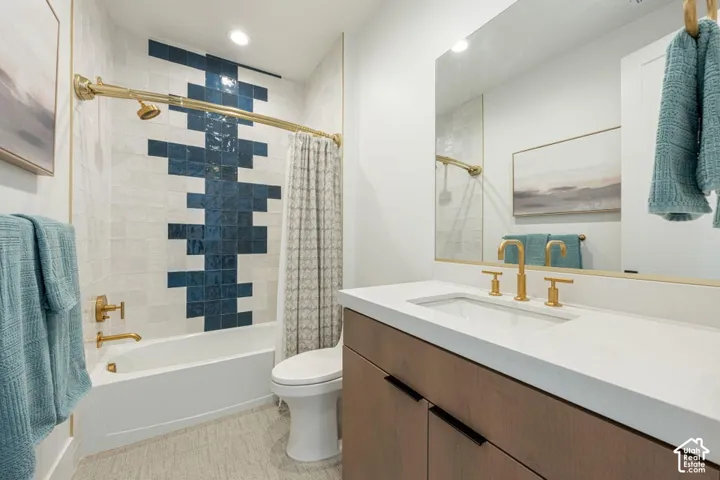 Bathroom featuring a built-in tub with gold-finish fixtures, a tiled shower surround with a decorative blue and white pattern, a wood-finish vanity with a white countertop, and a large mirror