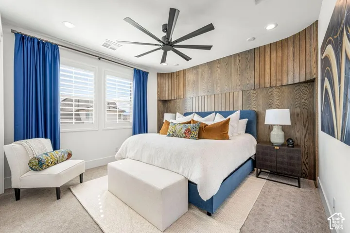 Recessed lighting, wood-paneled accent wall, dual windows with plantation shutters, ceiling fan, and carpeted flooring
