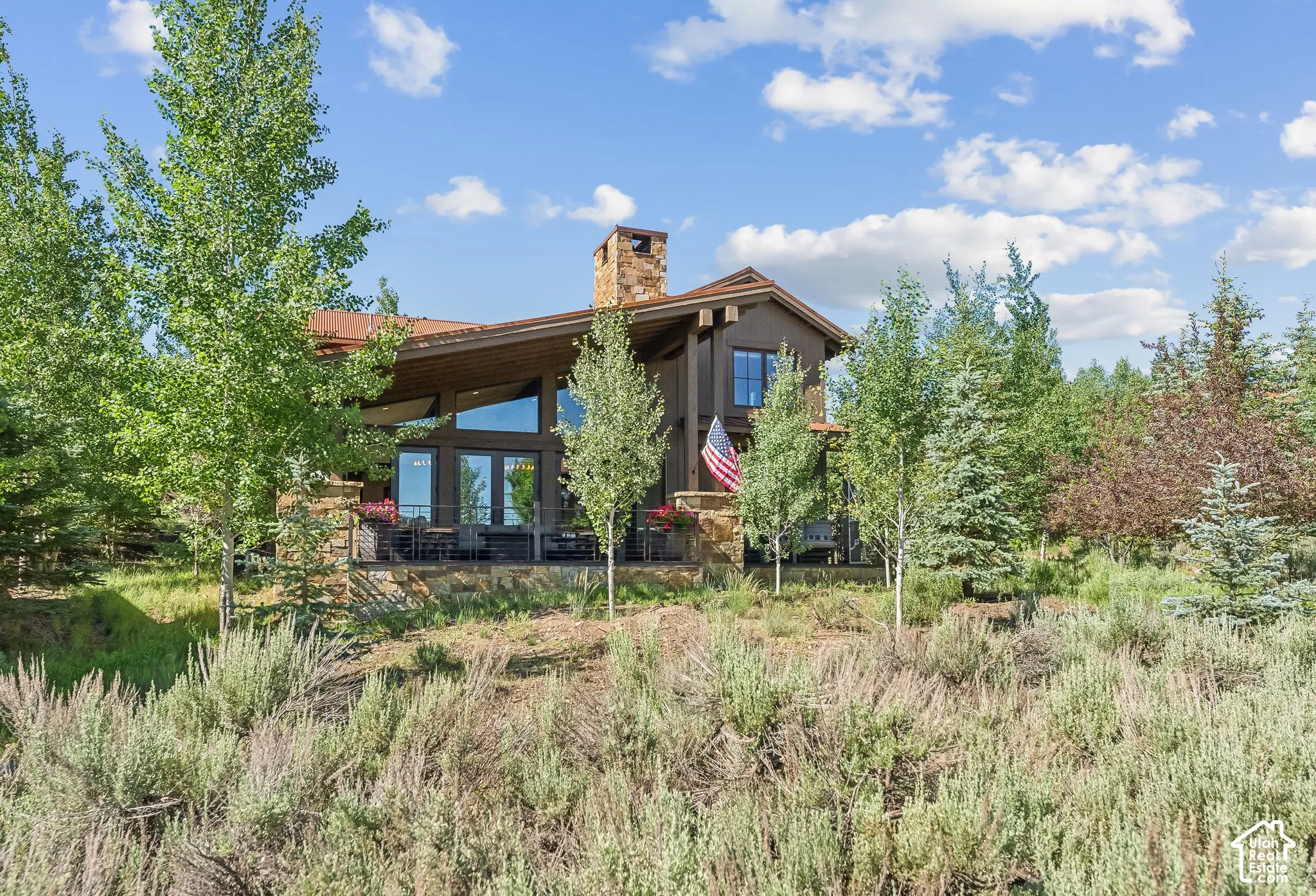 Two-story residence featuring a stone chimney, deep brown exterior, and a prominent deck with ample seating