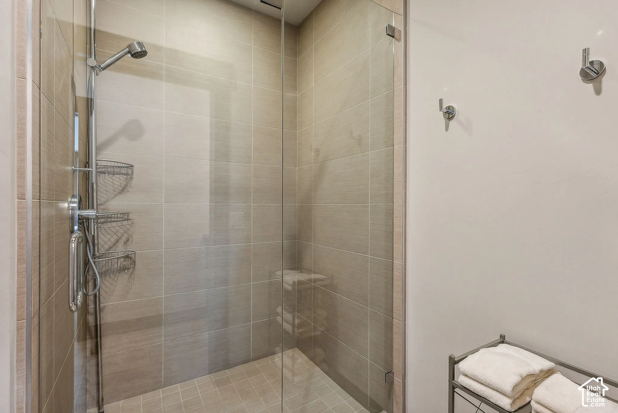 Glass-enclosed shower with full-height tile surround, integrated showerhead, and wall-mounted hooks