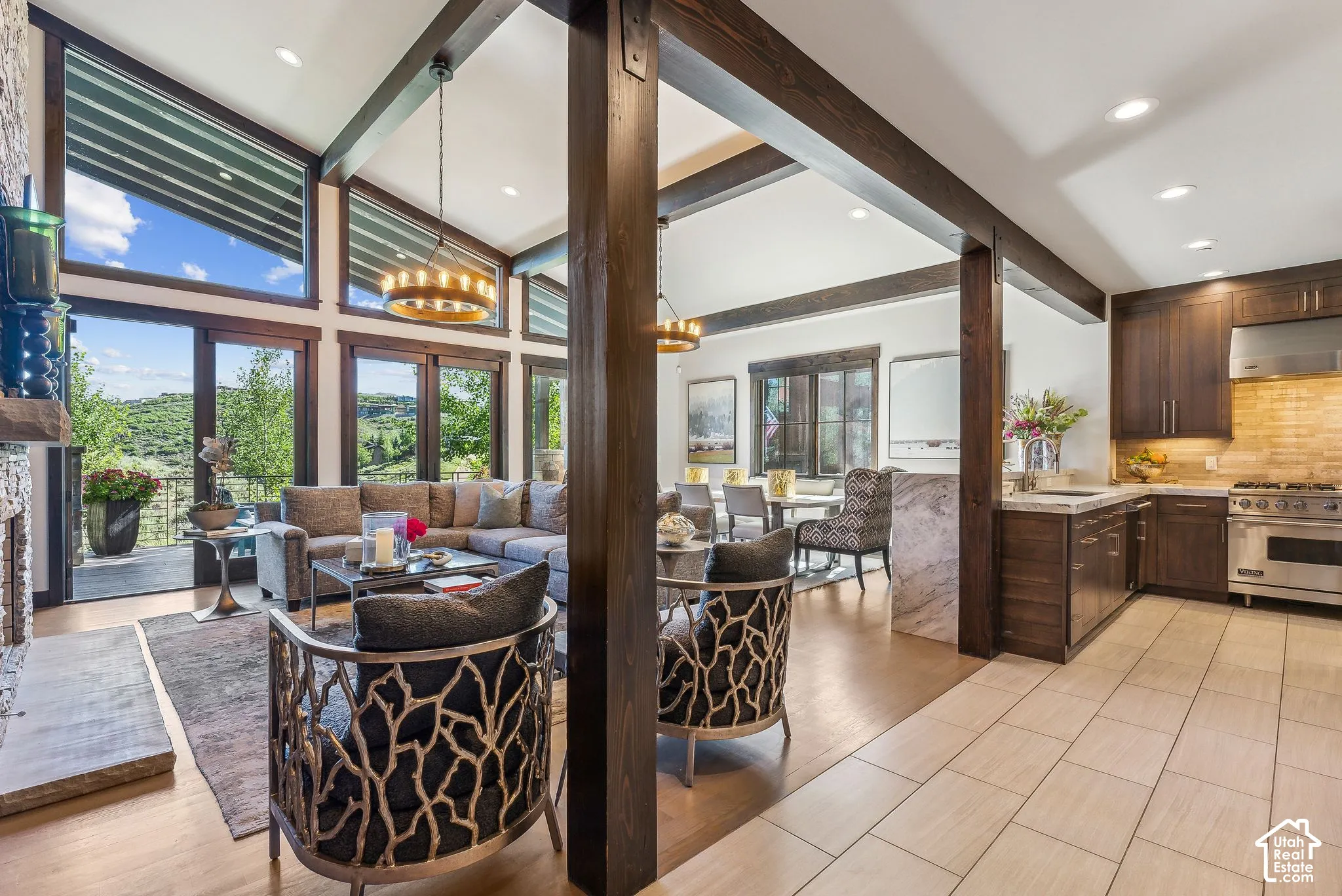 Expansive living space featuring vaulted ceilings with exposed wood beams, a stone fireplace, and a wall of windows