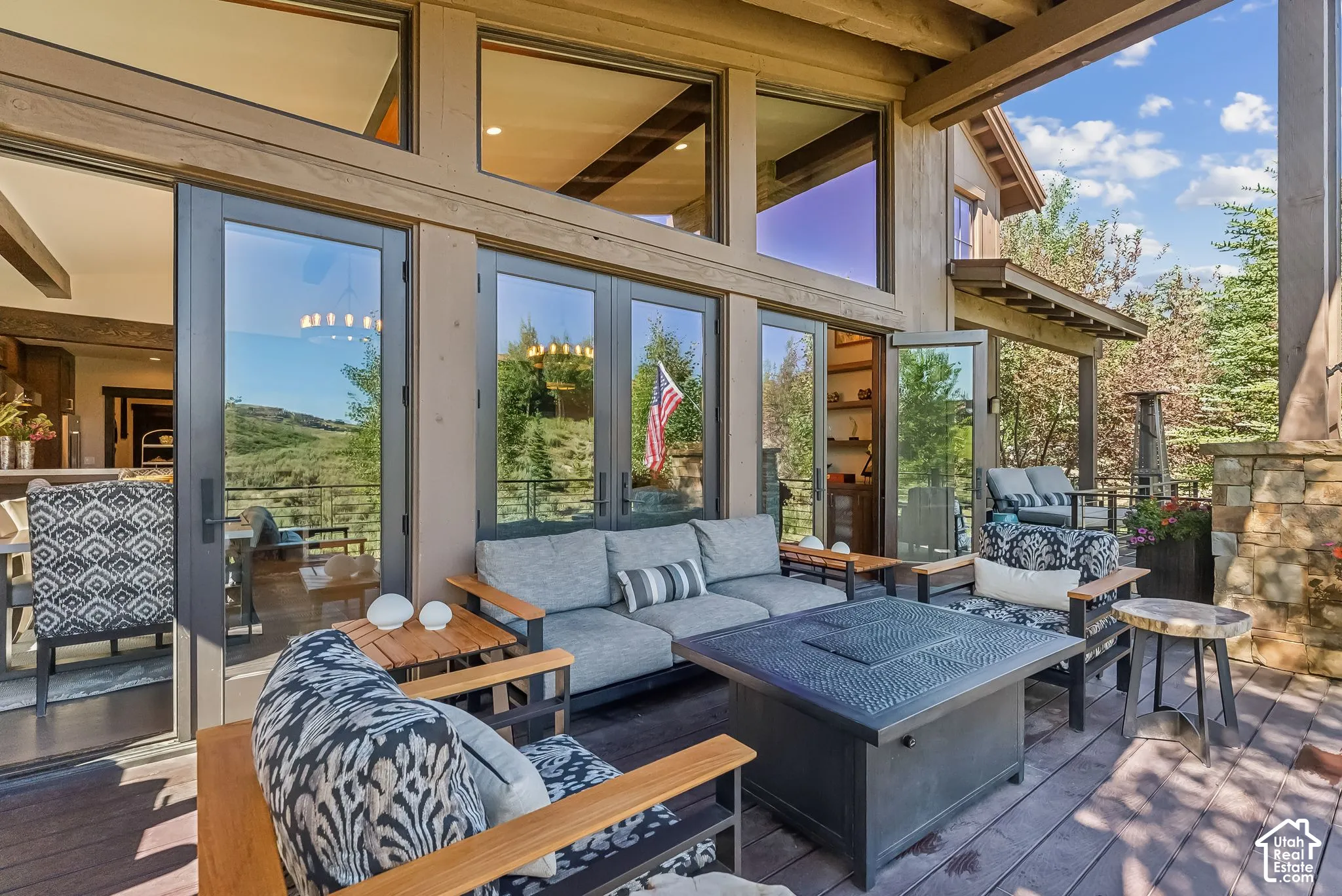 Expansive covered patio with floor-to-ceiling glass walls and wood-beam ceiling, anchored by a built-in fire pit with seating area