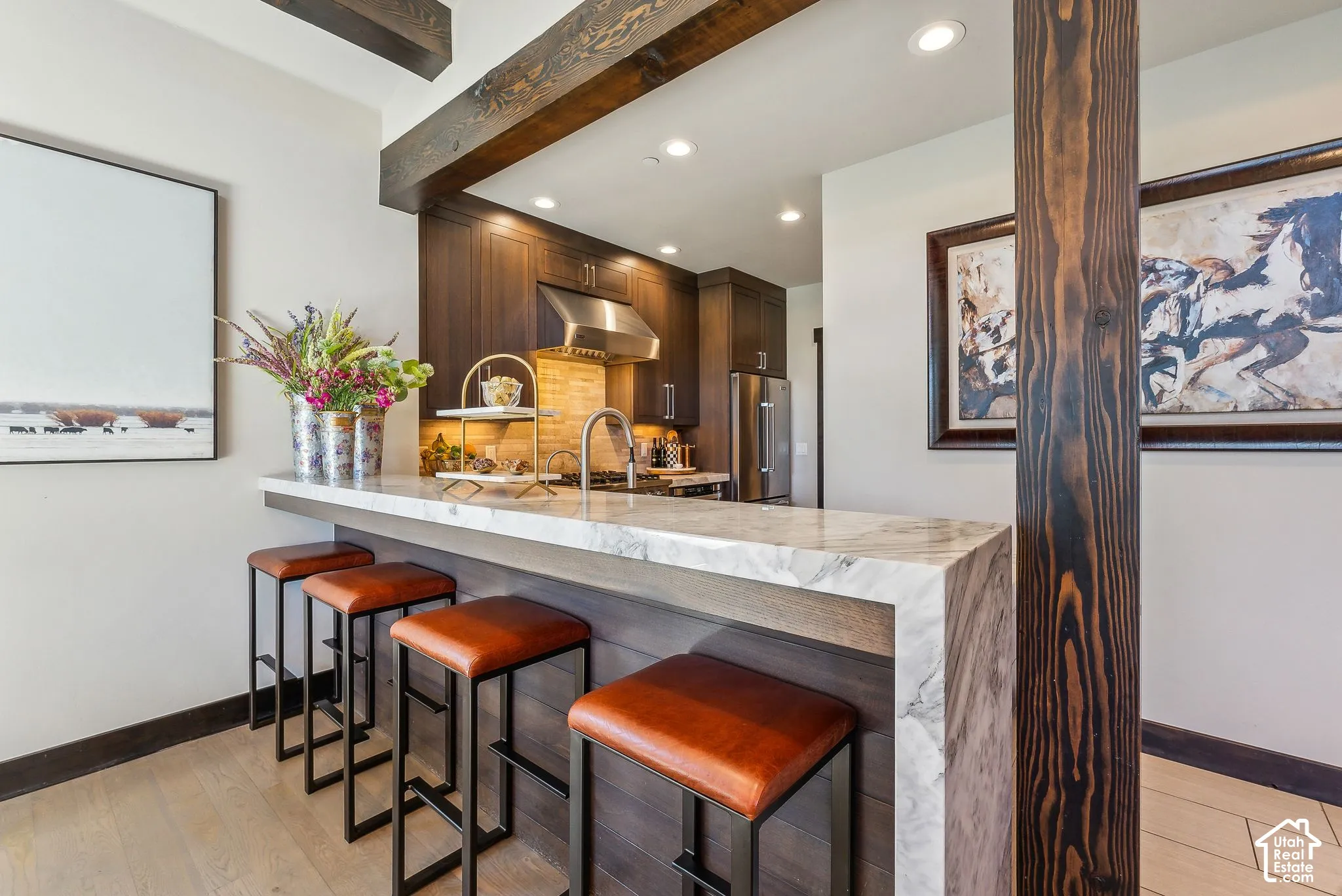 Kitchen featuring a breakfast bar with a waterfall countertop, wood-finish cabinetry, stainless steel appliances, and wood-finish flooring