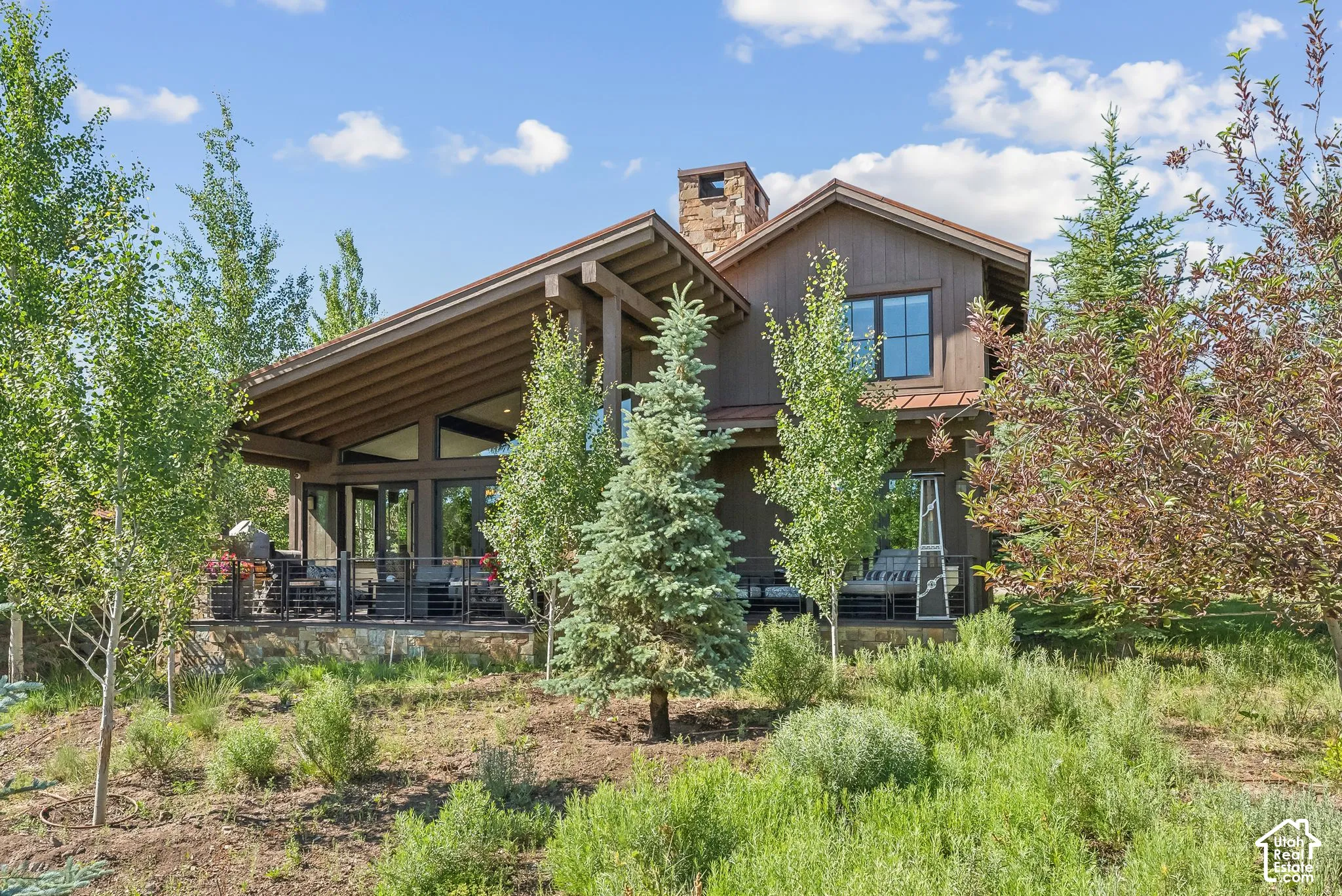 Wood-sided exterior featuring a stone chimney, a gabled roof, and a covered patio with metal railings
