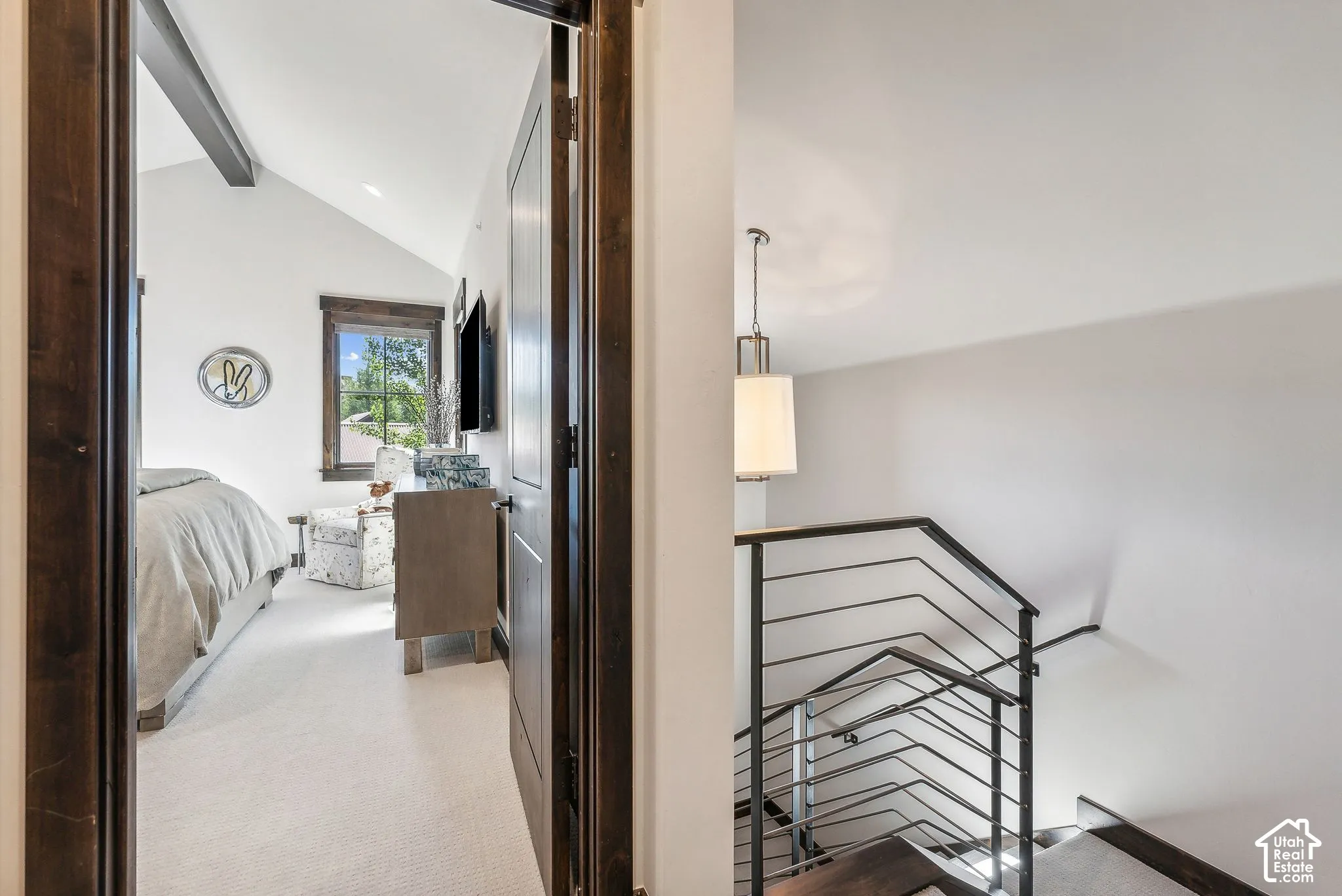 White vaulted ceiling with exposed wood beam, wood-trimmed window, and light-colored carpeting