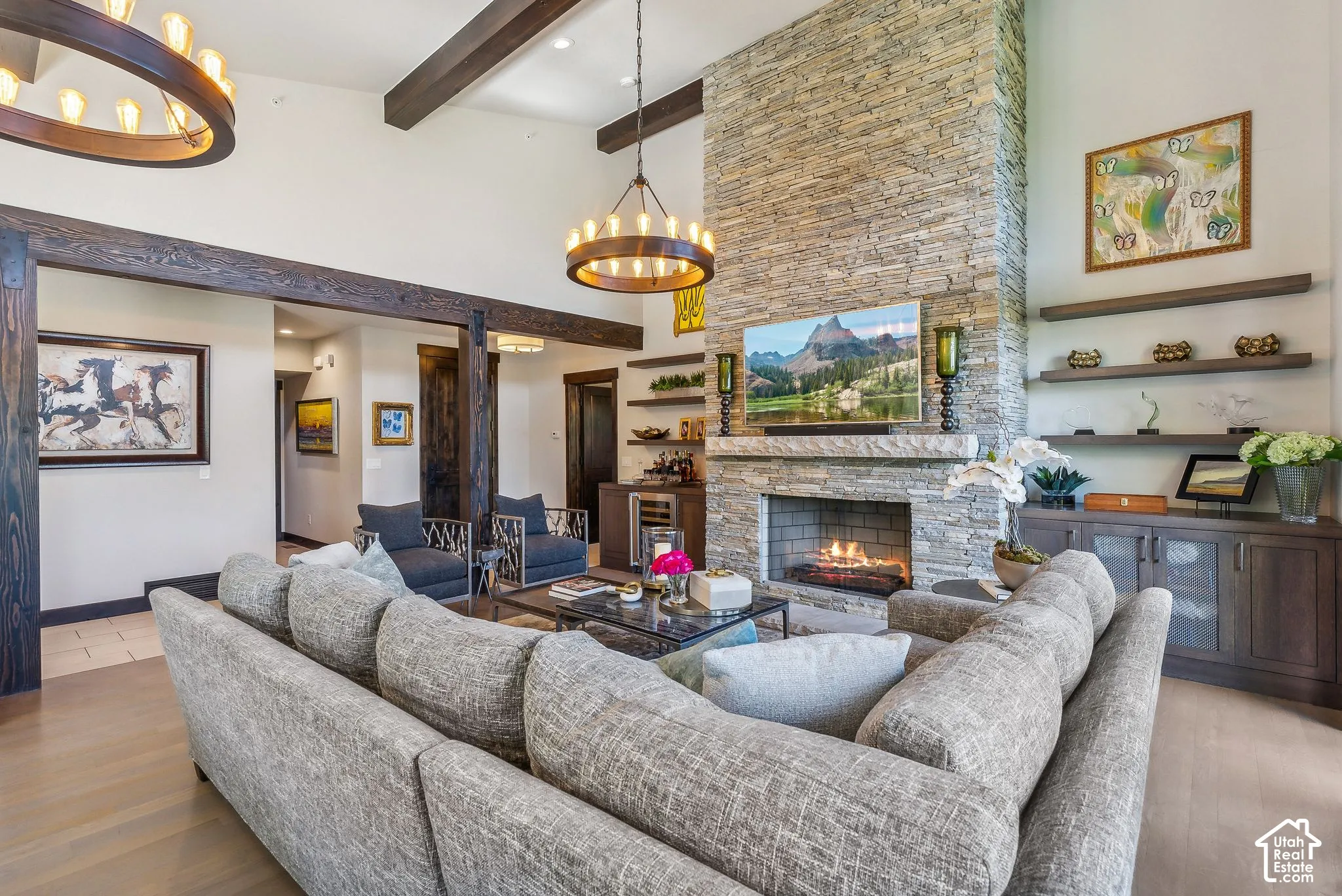 Vaulted ceiling with exposed wood beams, stone fireplace, built-in shelving, wood-finish flooring, and a stone accent wall
