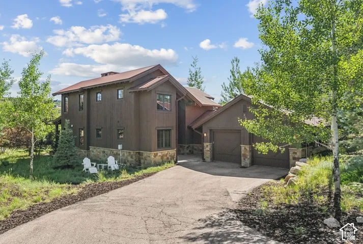 Driveway leading to an attached garage with a dark wood-finish door, stone accents on the facade, and a complementary brown roof