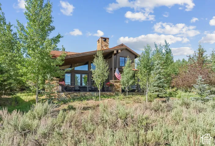 Two-story residence featuring a stone chimney, deep brown exterior, and a prominent deck with ample seating