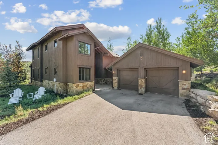 Exterior featuring wood siding, stone accents, and a dual-bay garage with carriage-style doors