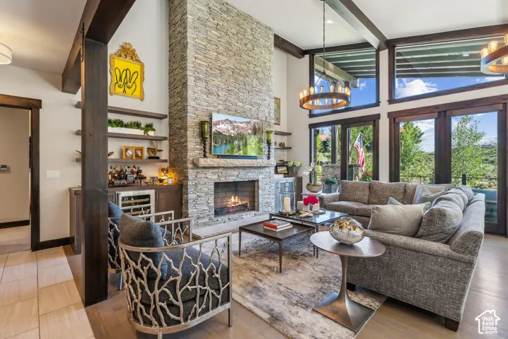 Stone-clad fireplace feature wall, built-in wet bar with wine cooler, wood-finish flooring, exposed wood beams, and a wall of windows