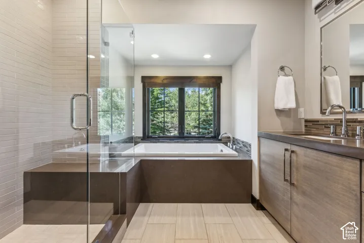 Built-in soaking tub with surrounding tile, glass-enclosed shower with tile surround, wood-finish vanity with countertop, and large framed mirror