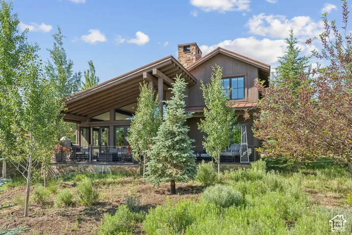 Wood-sided exterior featuring a stone chimney, a gabled roof, and a covered patio with metal railings