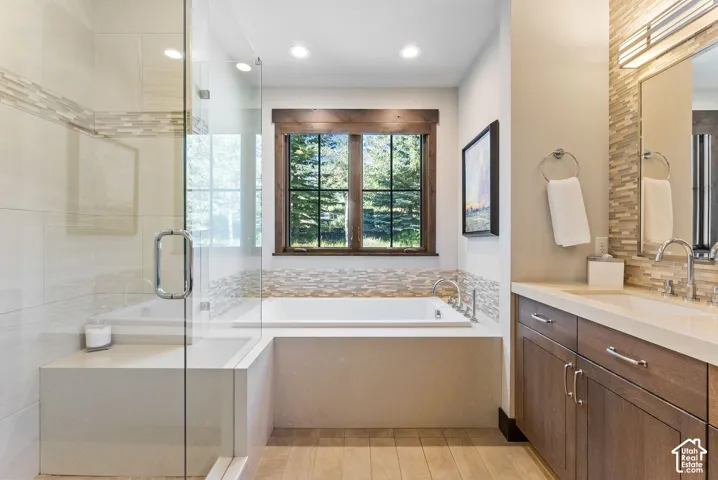 Glass-enclosed shower with integrated bench, built-in soaking tub, wood-finish window frame, vanity with dual sinks, and light wood-finish flooring