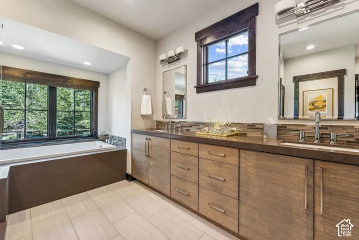 Built-in soaking tub, wood-finish vanity with ample storage, dual undermount sinks, and a mosaic tile backsplash