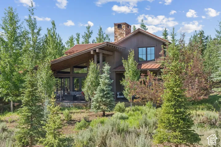Wood-sided exterior with a stone chimney, extensive natural landscaping, and a covered porch
