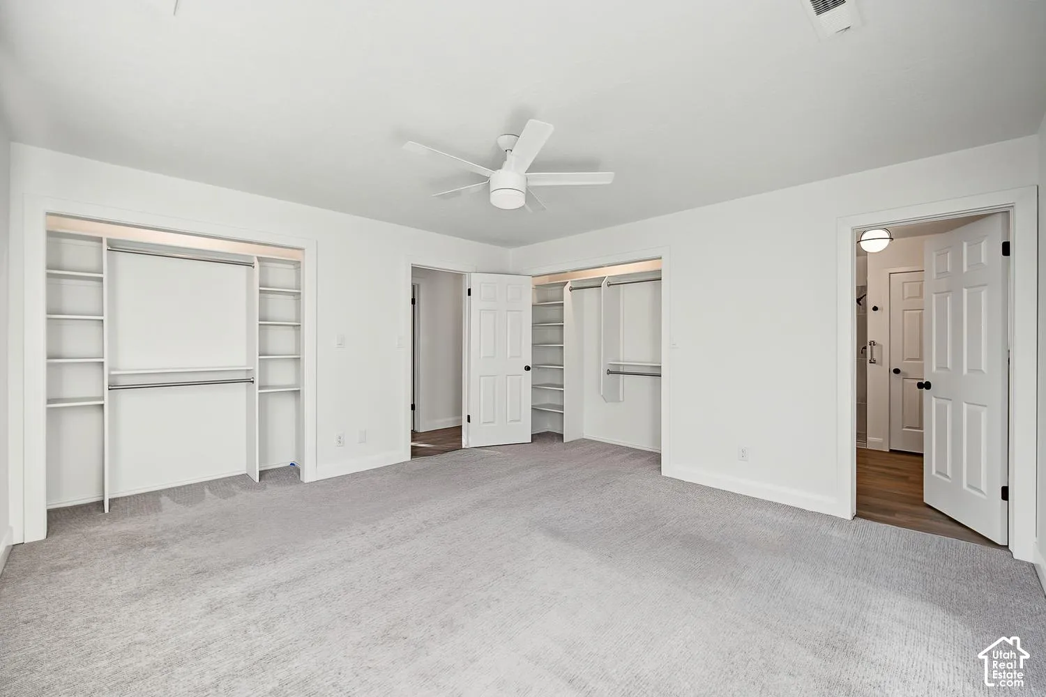 Spacious room featuring light gray carpeting, a ceiling fan, and built-in closet organization with shelving and hanging rods