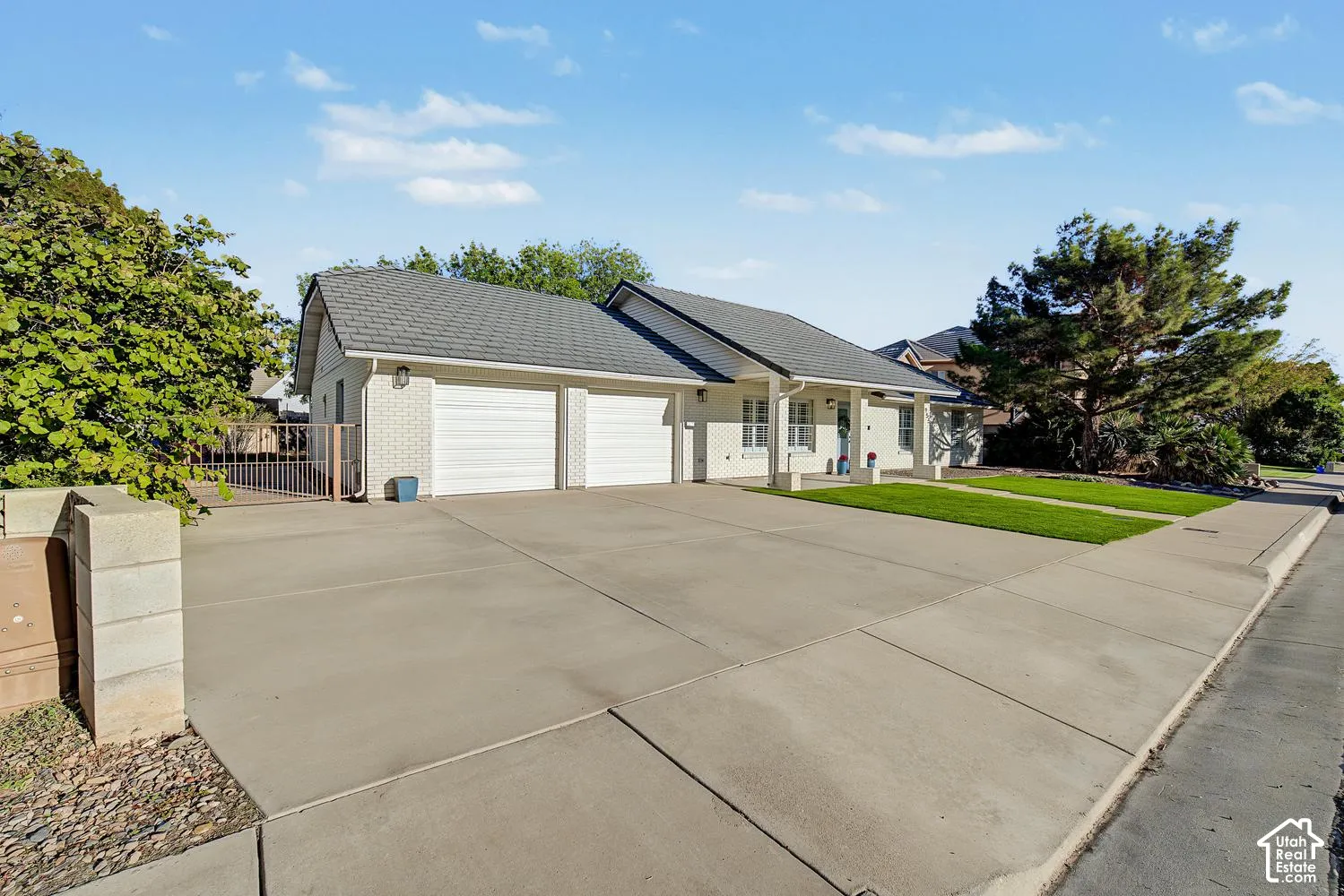 Expansive concrete driveway with multiple garage bays, mature landscaping with established trees, and a single-story ranch-style residence featuring a gabled roof and neutral exterior finishes