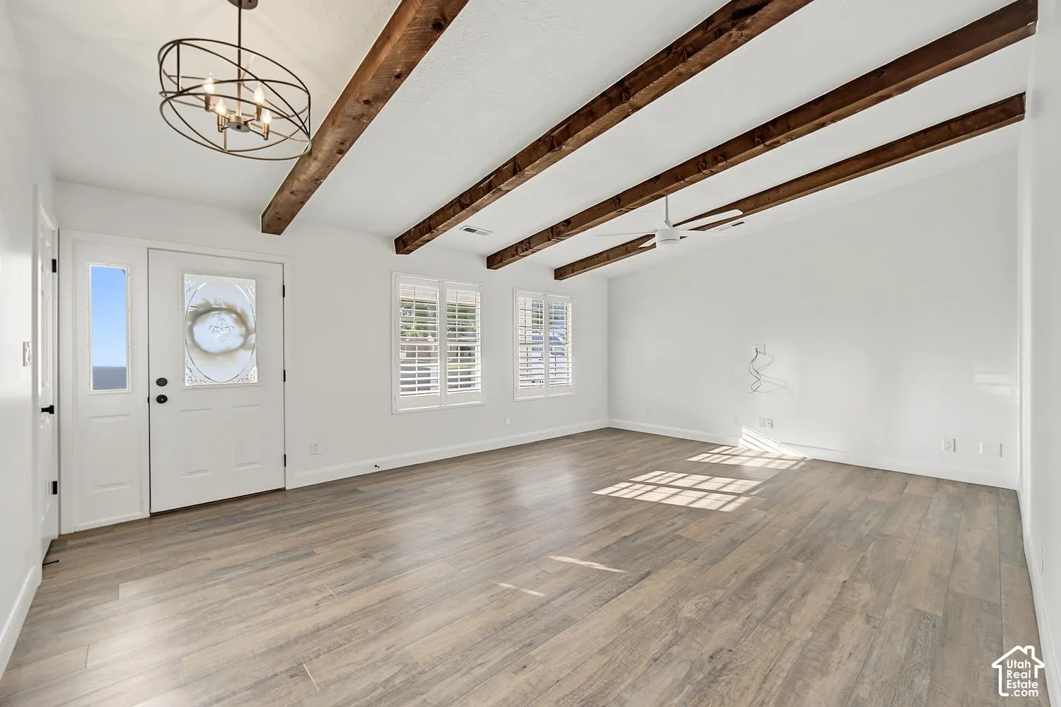 Vaulted ceilings with exposed wood beams, wood-finish flooring, plantation shutters, and a decorative chandelier