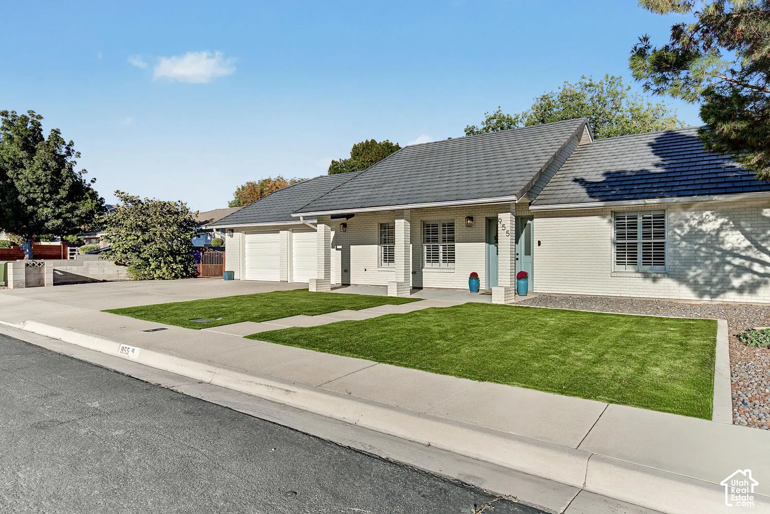 White brick exterior with a dark shingle roof, featuring a two-car garage, established landscaping, and a concrete driveway