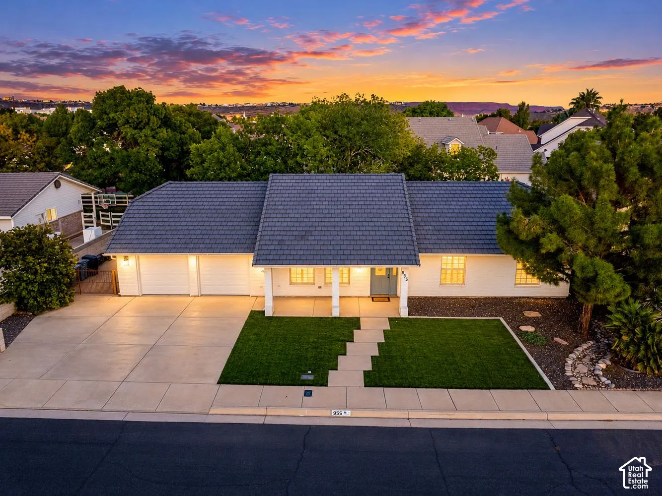 White exterior with a dark-tiled roof, featuring a two-car garage, a covered front entry with columns, and a landscaped front yard with artificial turf