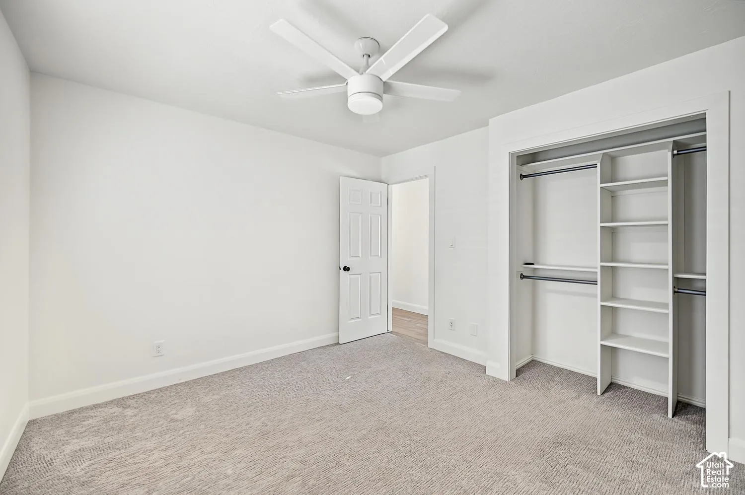 Neutral-toned wall-to-wall carpeting, white walls, and a ceiling fan with integrated lighting