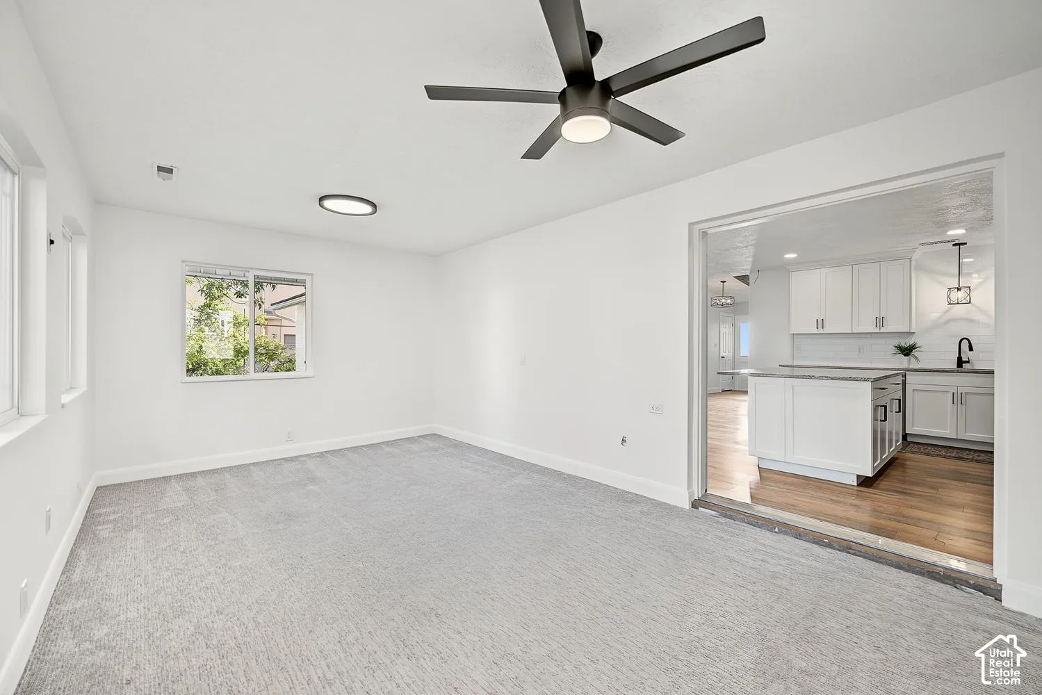 Spacious room featuring light gray carpeting, multiple windows, a modern ceiling fan, and a flush-mount overhead light