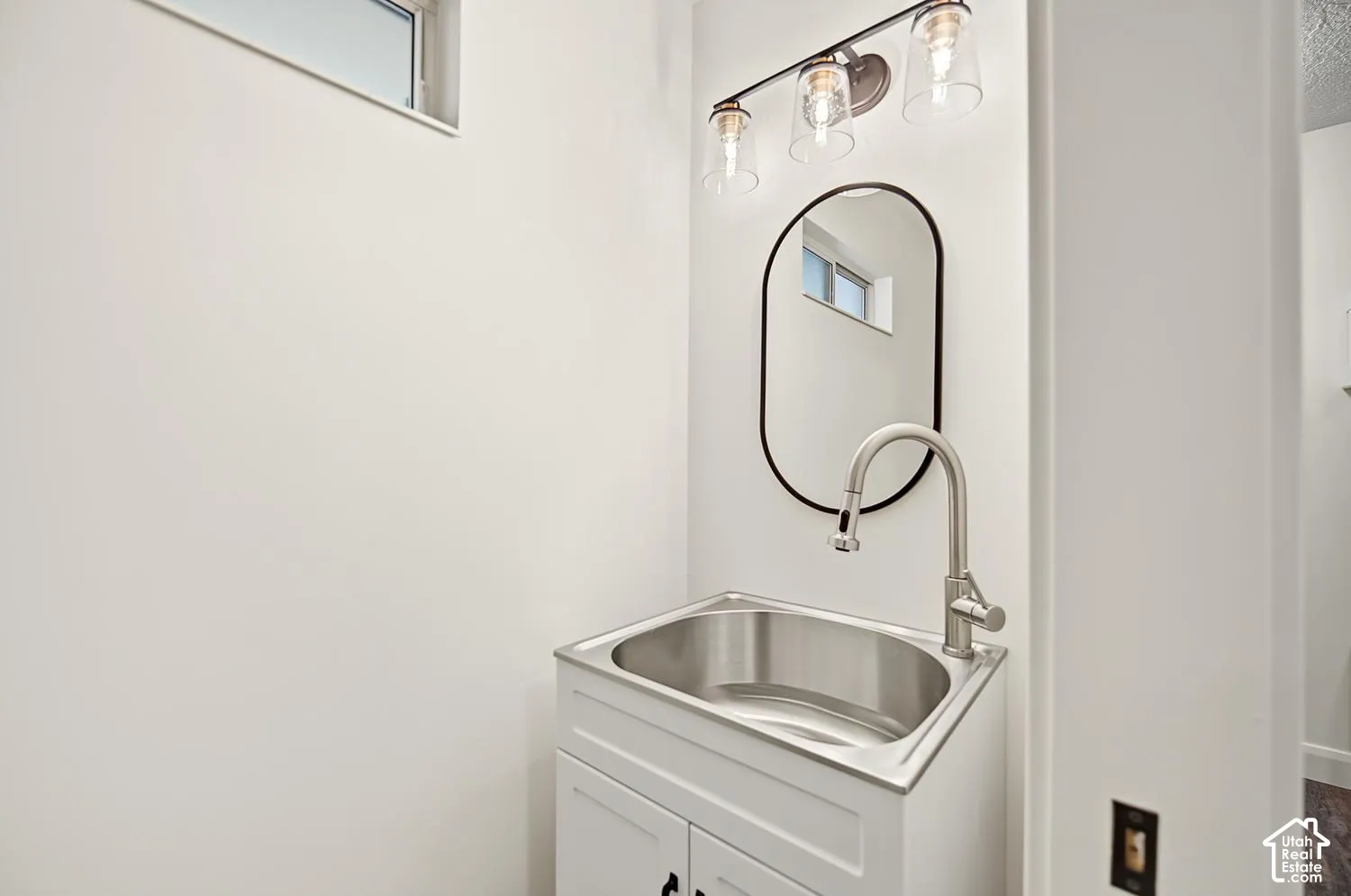 Modern powder room featuring a stainless steel rectangular vessel sink, white cabinetry with soft-close drawers, arched black-framed mirror, brushed nickel gooseneck faucet, and contemporary pendant lighting with clear glass shades