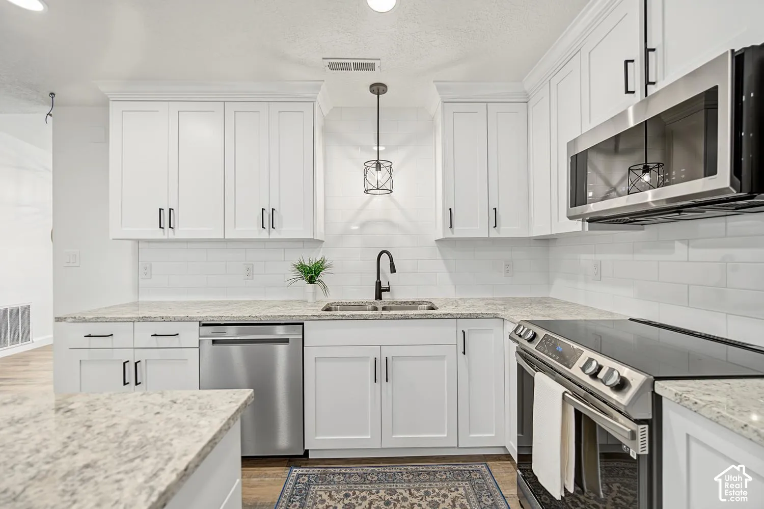 White shaker-style cabinetry with matte black hardware, stainless steel appliances, a subway tile backsplash, light-toned countertops, and a stainless steel sink with a gooseneck faucet