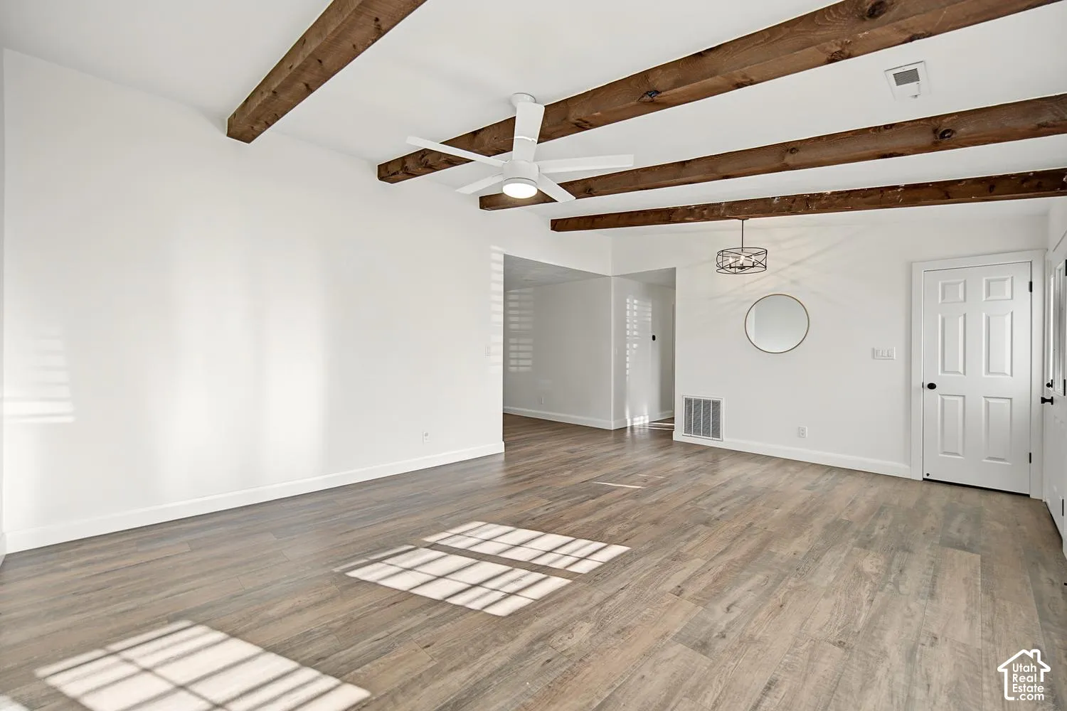Vaulted ceiling with exposed wood beams, wood-finish flooring, white ceiling fan, and white paneled door