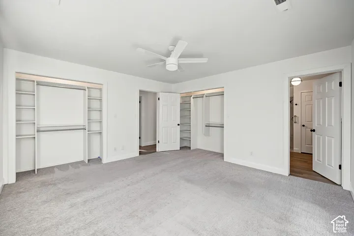 Spacious room featuring light gray carpeting, a ceiling fan, and built-in closet organization with shelving and hanging rods