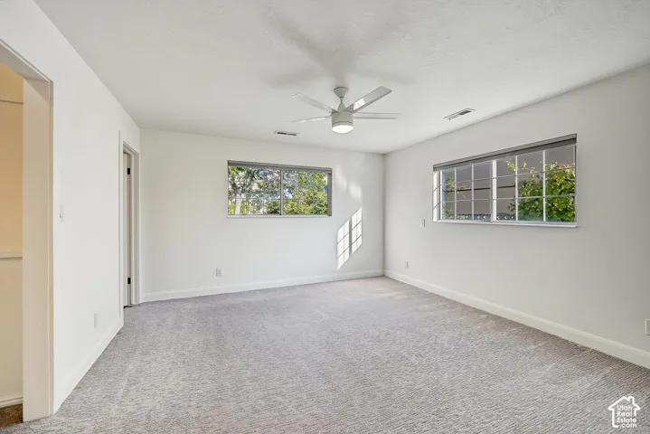 Light gray carpeting, white walls, two windows, and a ceiling fan