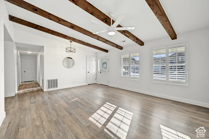 Wood-finish flooring, exposed ceiling beams, white interior doors, and multiple windows with plantation shutters