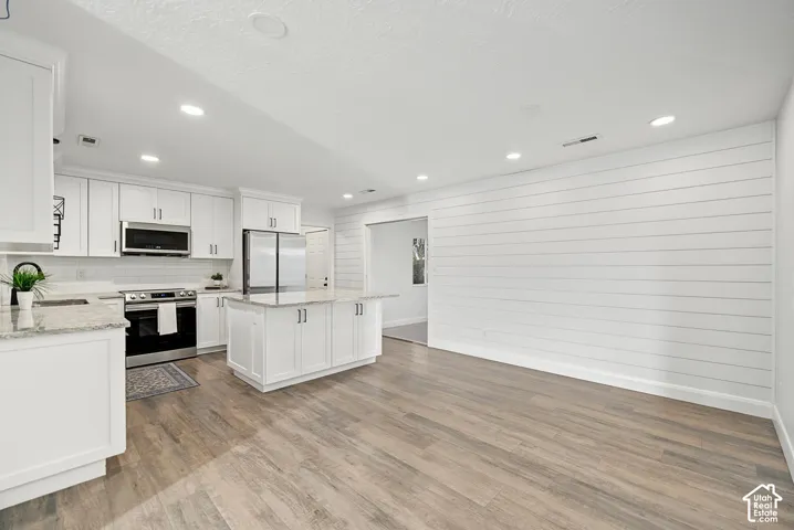 Open-concept kitchen featuring white cabinetry, stainless steel appliances, a center island, and light-toned wood-finish flooring
