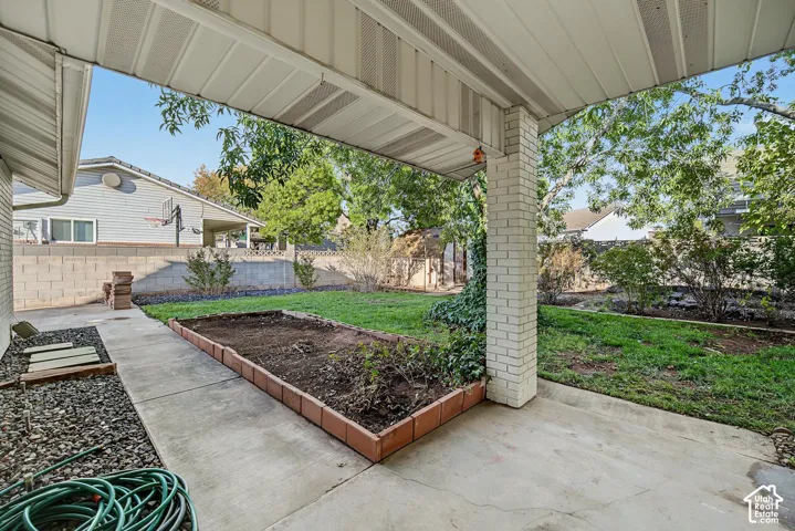 Covered patio with brick column, concrete patio, and a raised garden bed