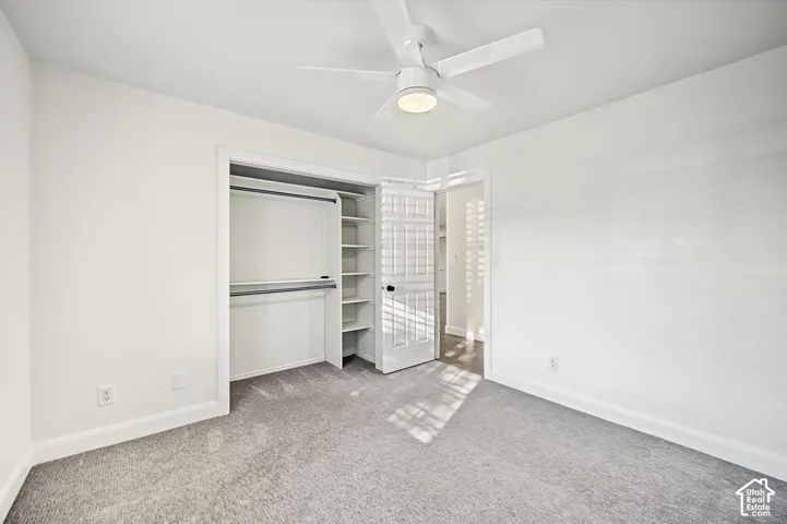Plush carpet flooring, integrated ceiling fan with lighting, white interior walls, and built-in closet shelving