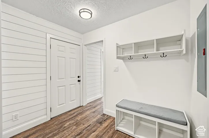Wood-finish flooring, white shiplap wall paneling, built-in shelving with coat hooks, white panel door, and overhead flush-mount lighting