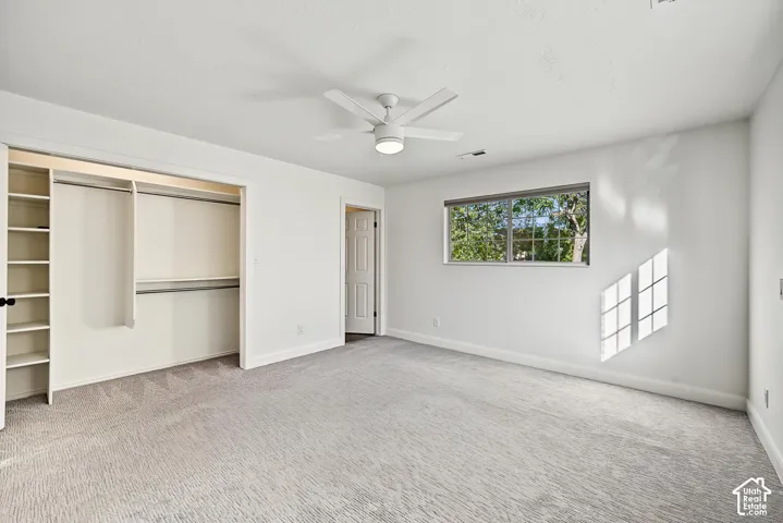 White walls, light-colored carpet, a ceiling fan, a window, and an open closet with built-in shelving