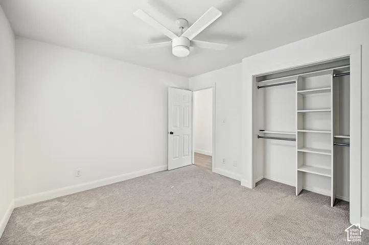 Neutral-toned wall-to-wall carpeting, white walls, and a ceiling fan with integrated lighting