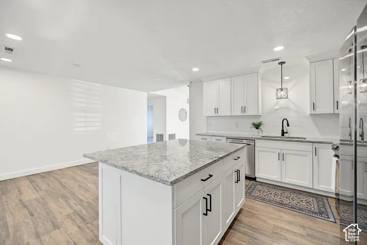 Kitchen featuring a large island with a stone-finish countertop, white cabinetry, integrated sink with a matte black faucet, and wood-finish flooring