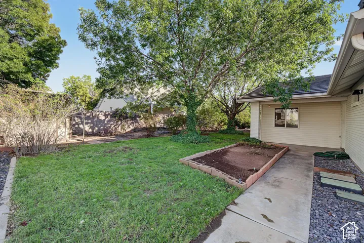 Expansive backyard featuring a mature tree, concrete pathway, decorative stone landscaping, raised garden bed, and a durable shingle roof