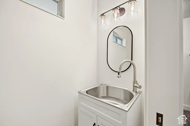 Modern powder room featuring a stainless steel rectangular vessel sink, white cabinetry with soft-close drawers, arched black-framed mirror, brushed nickel gooseneck faucet, and contemporary pendant lighting with clear glass shades