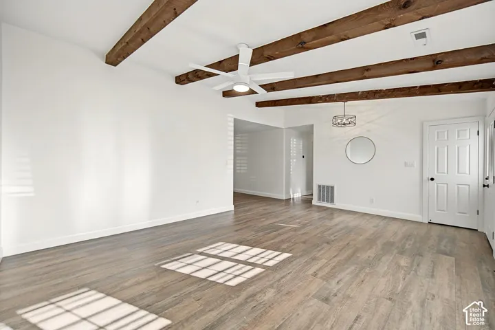 Vaulted ceiling with exposed wood beams, wood-finish flooring, white ceiling fan, and white paneled door