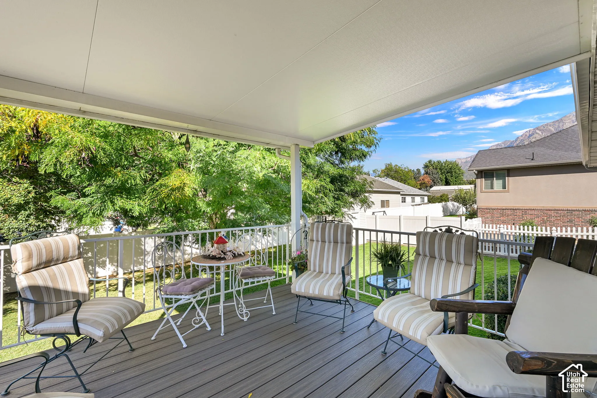Covered deck featuring composite decking, white railing, and a mature tree backdrop